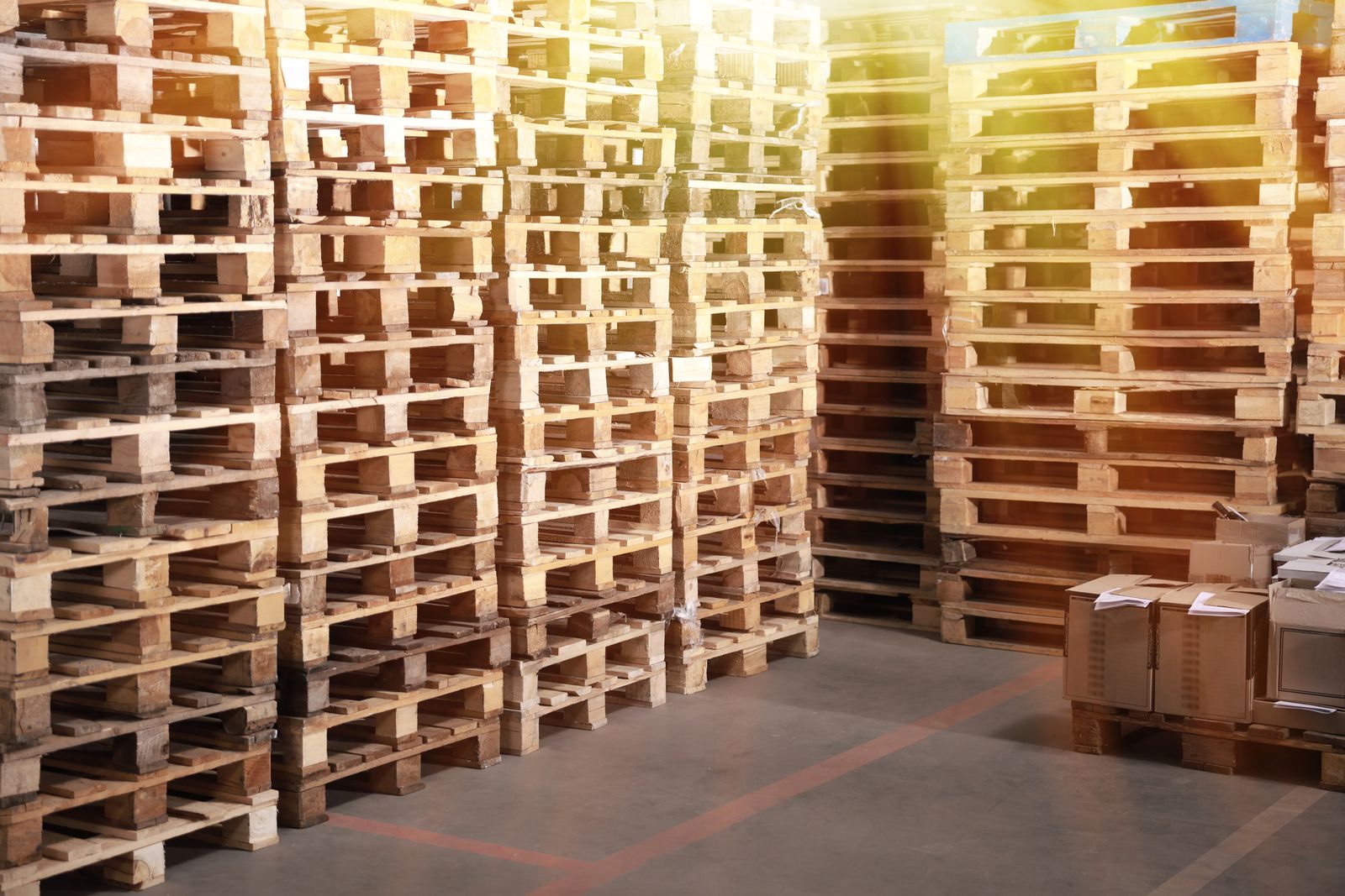 Photograph of wooden pallets stacked in a warehouse, representing used pallet supply; condition and grade confirmed per enquiry