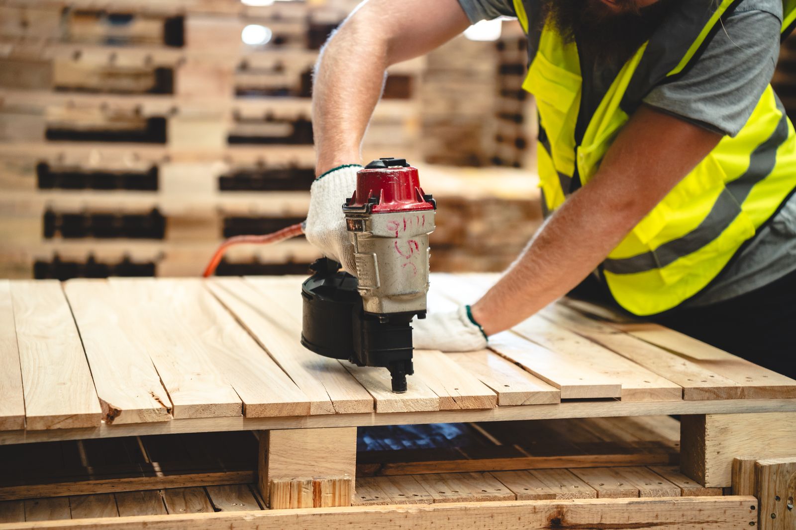 Illustrative stock photograph of a worker nailing timber boards onto a pallet with a nail gun